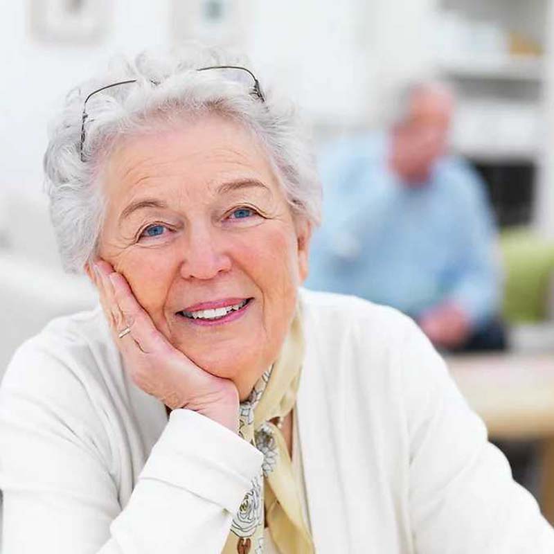 an elderly woman resting her chin on her hand and smiling