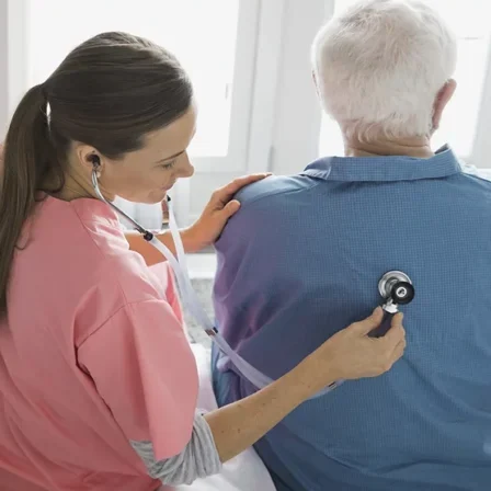 a doctor placed a stethoscope on the back of an elderly man to hear his lungs.